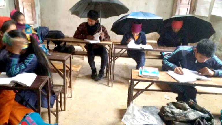 कक्षाकोठामा पानी चुहिएपछि छाता आढेर पढ्दै रोल्पाको रुन्टीगढी गाउँपालिकाको एक विद्यालय  ।